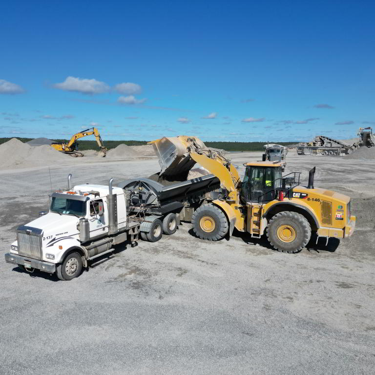 Caterpillar loader and truck with excavator background