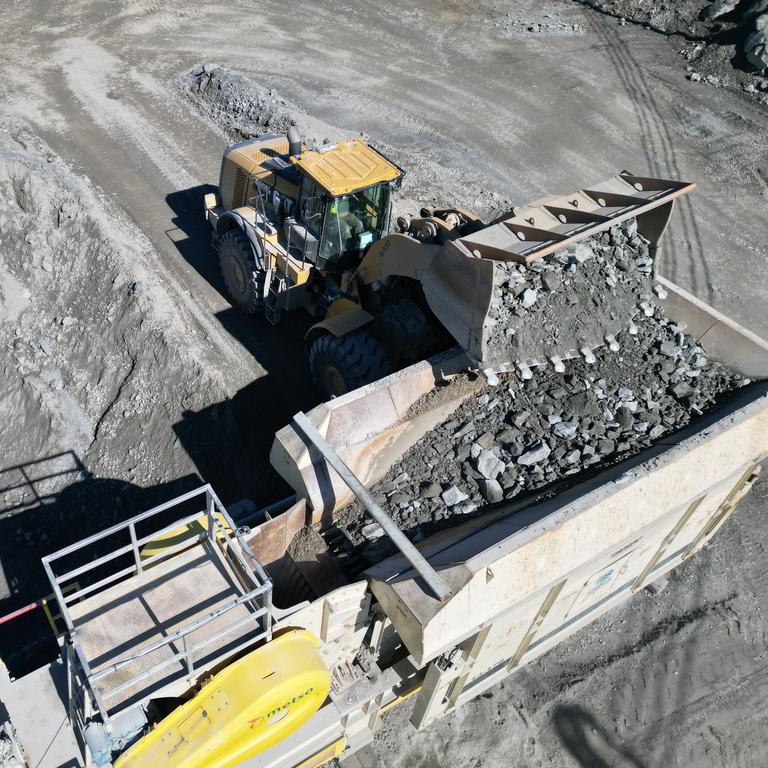 Loader dumping rocks into crusher hopper